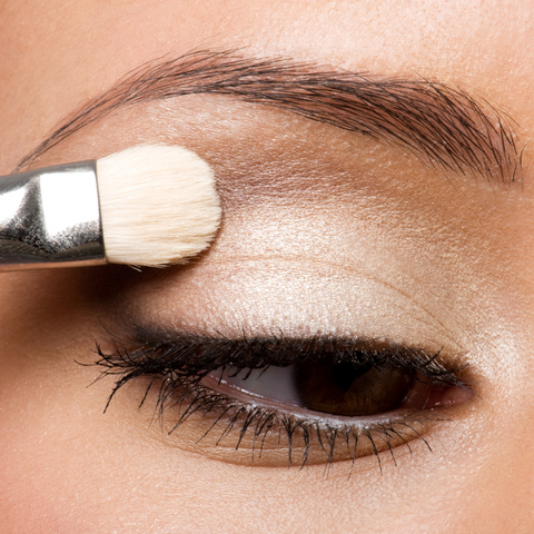 Close up image of woman's eye applying highlighter on eyelid