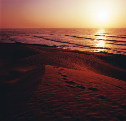 Sunset on a beach with footprints, reds, oranges and yellows.