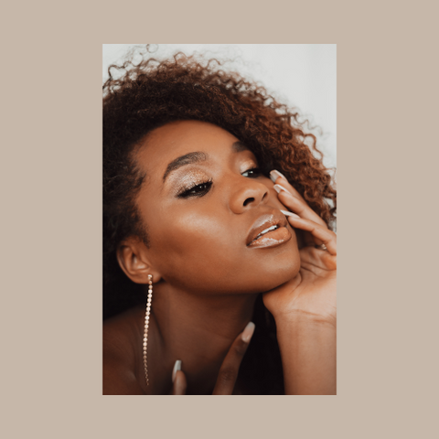 Black woman with curly hair with head in hand, shimmery makeup and nude lip