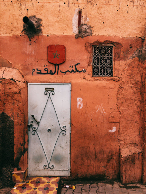 White door, Moroccan flag above door, worn orange wall