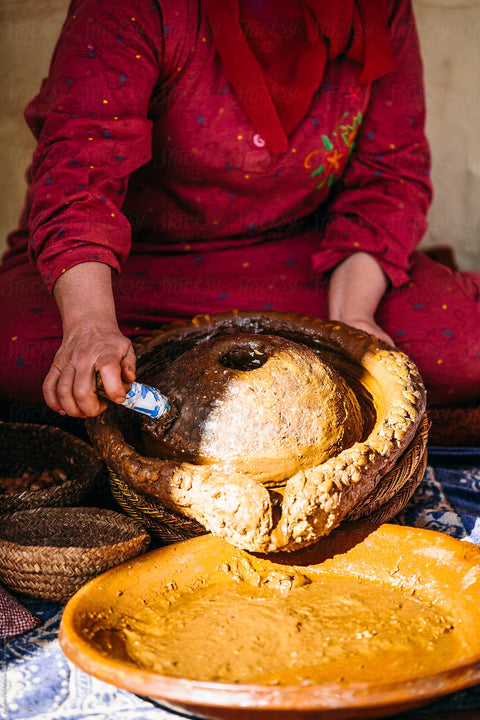 Woman in red dress processing argan oil by hand into clay pots